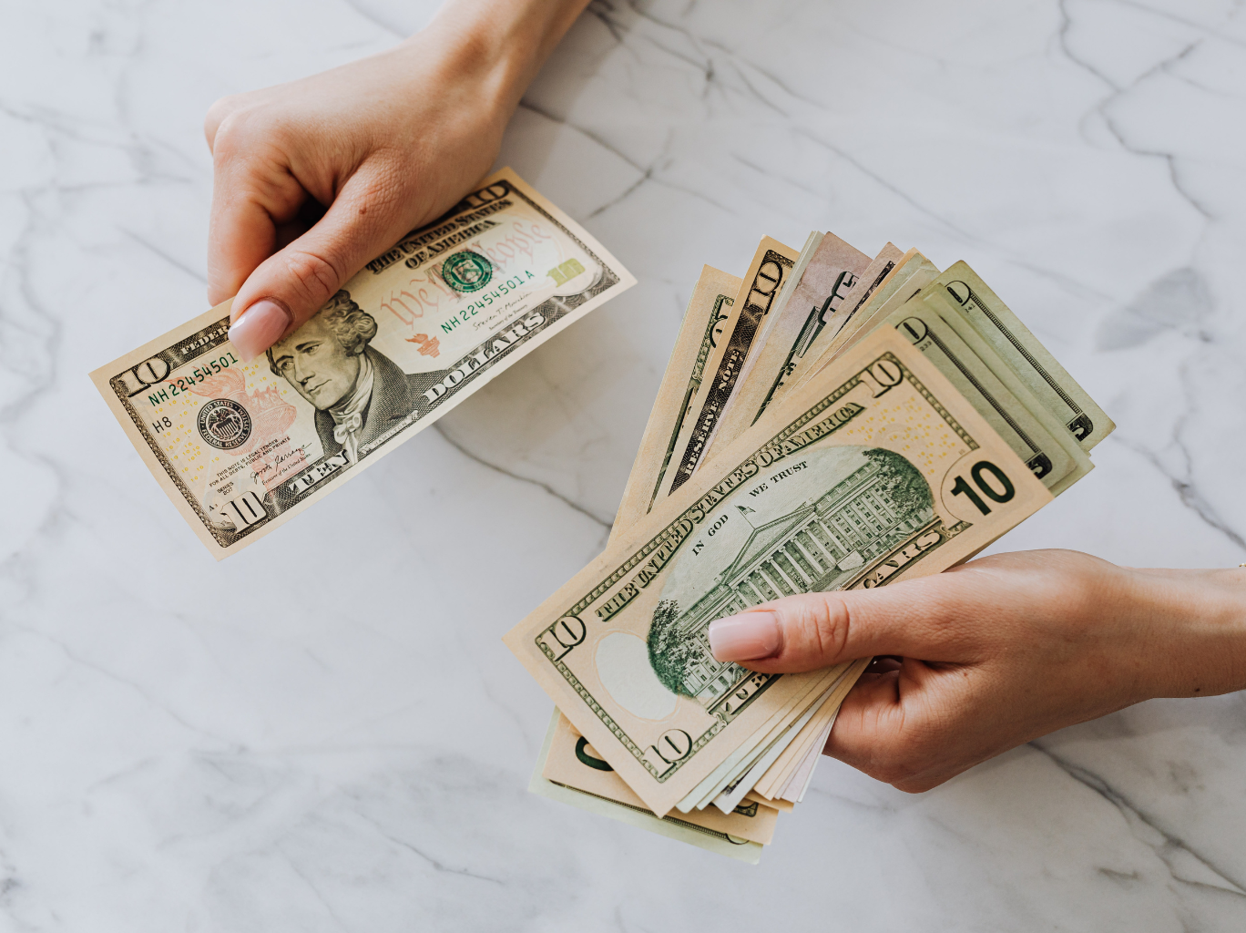 A female entrepreneur sitting at a desk, counting out ten-dollar bills carefully while learning about fair compensation and how to pay yourself.