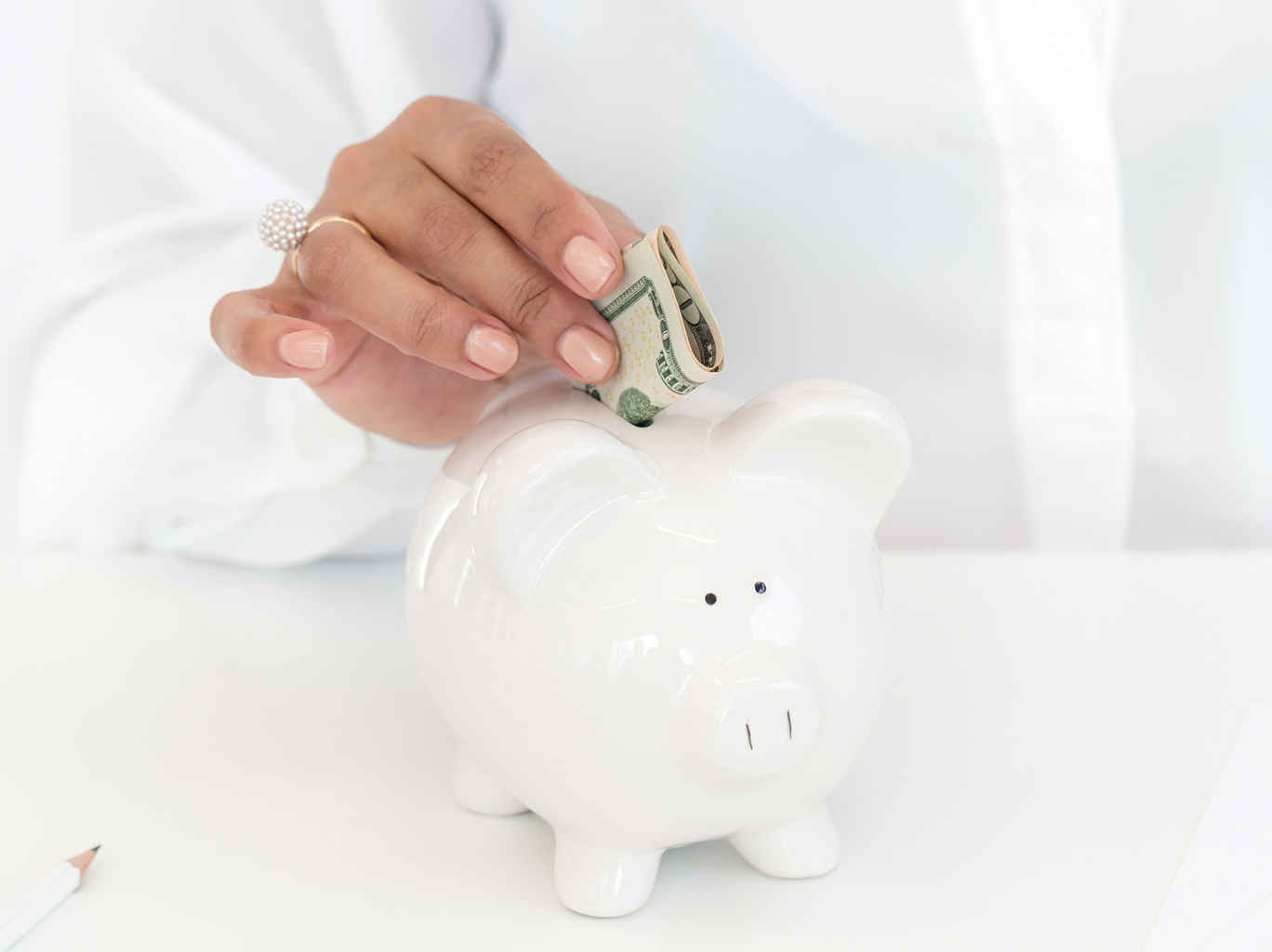 An entrepreneur who is thinking about the power of bootstrapping and self-funding her business placing cash into a white piggy bank.