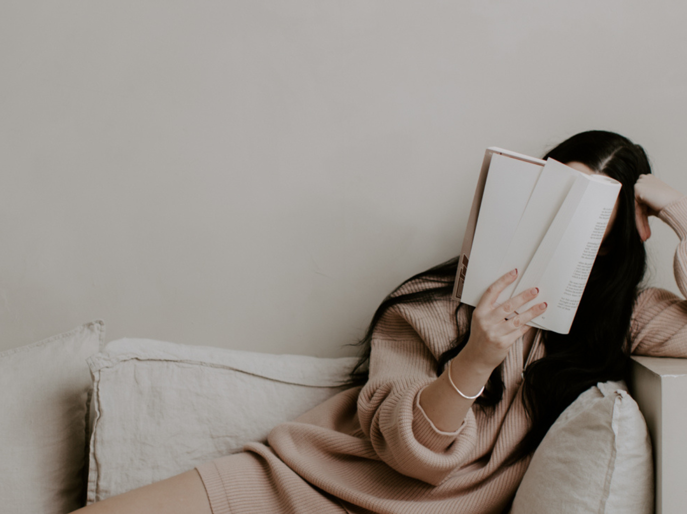 Woman sitting on couch holding up a book and reading notes